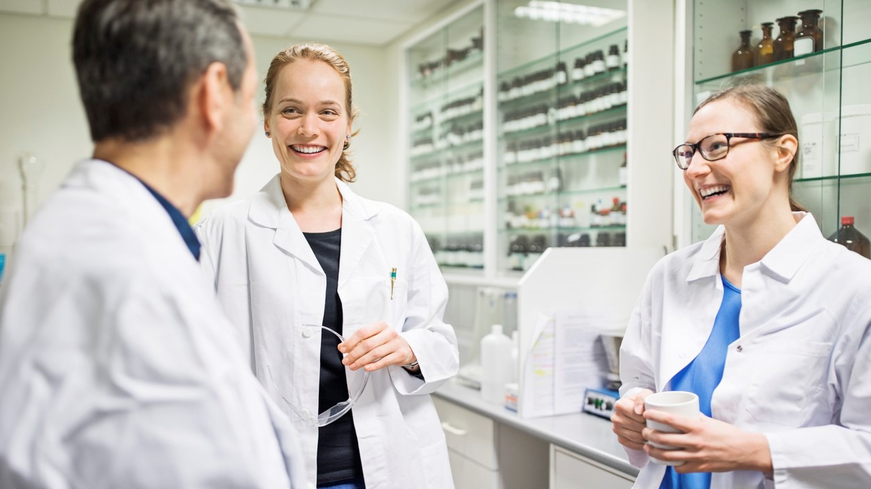 Happy scientists talking in laboratory. Smiling male and female pharmacists are wearing lab coats. Professionals are at pharmacy.